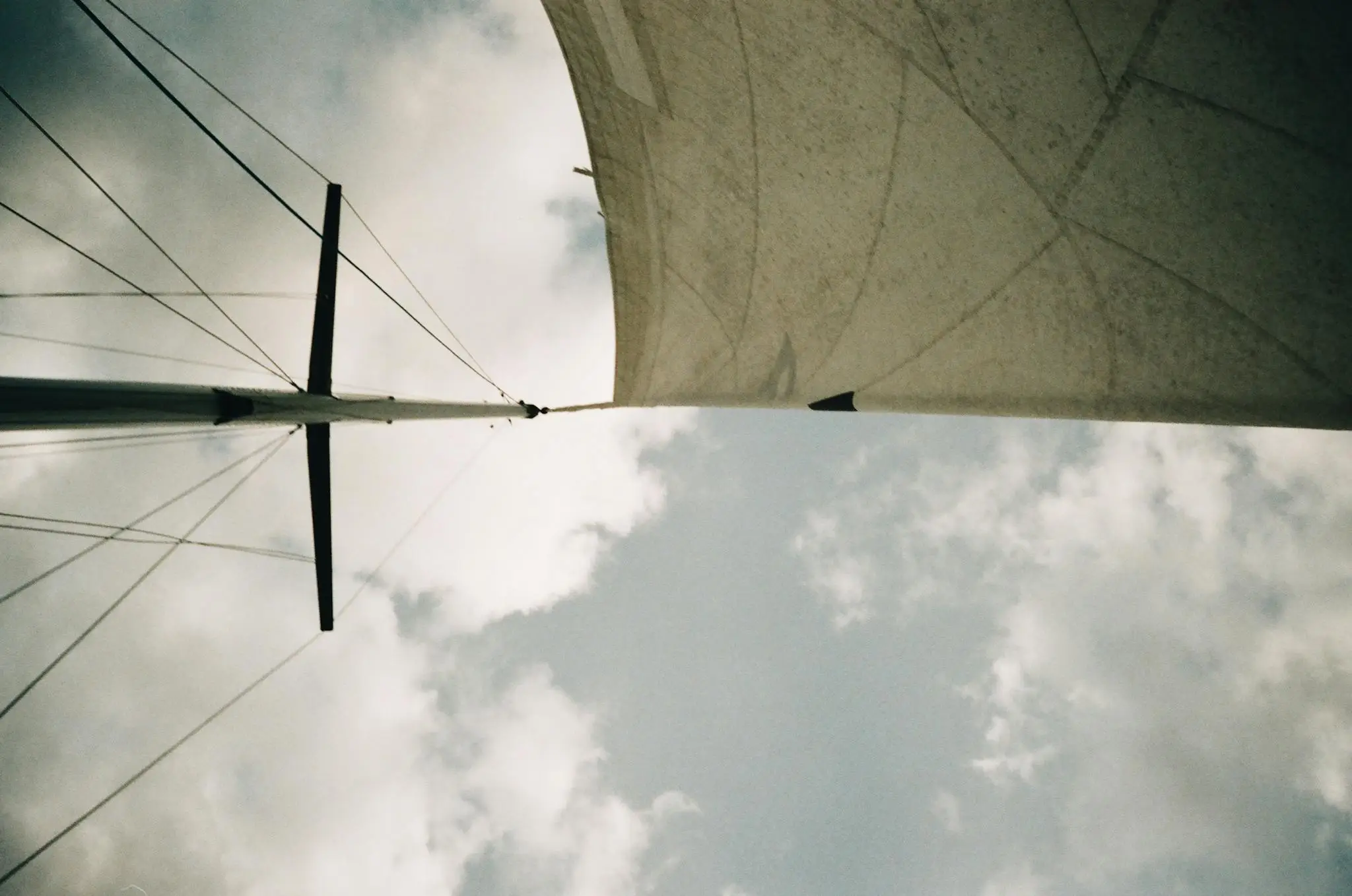 View of a sailing boat's mast and sail set against a backdrop of dramatic clouds, captured from below.